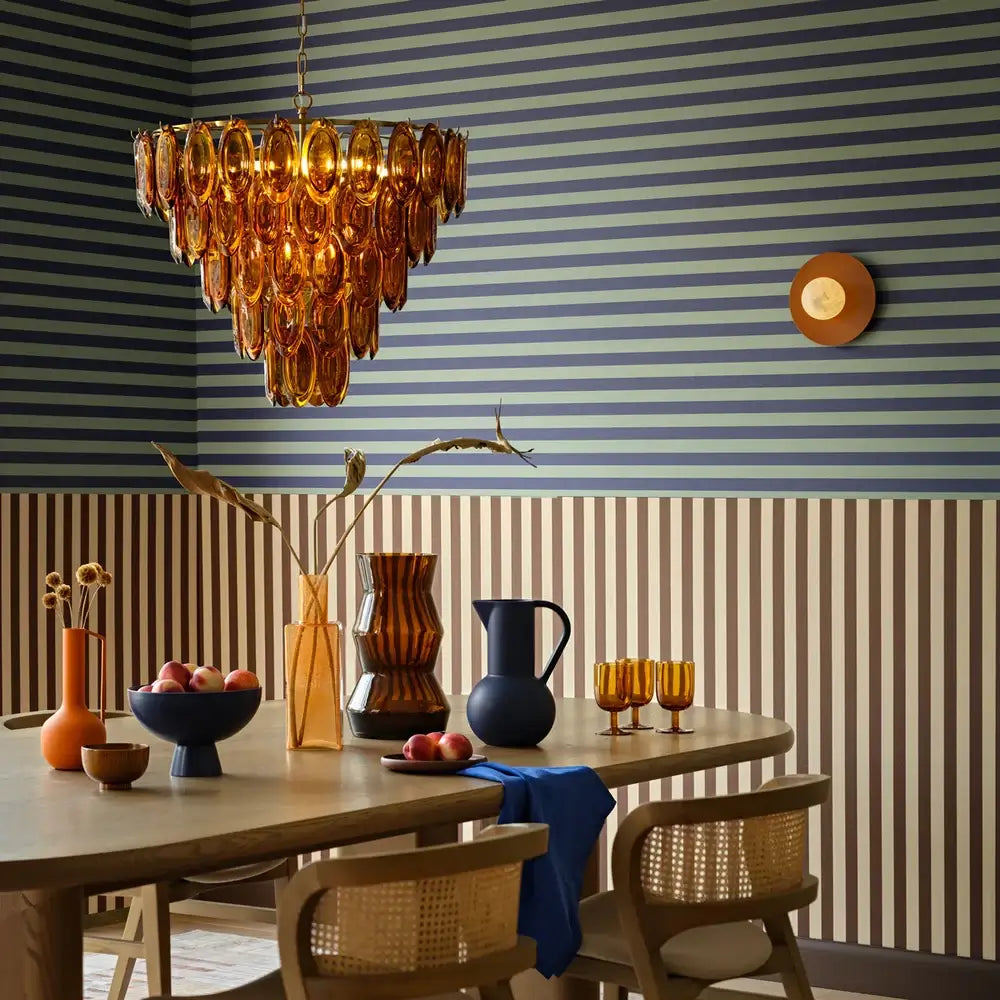 SALE Pooky Lyle Chandelier in amber glass hanging in a stylish dining room with decorative vases and striped wallpaper.