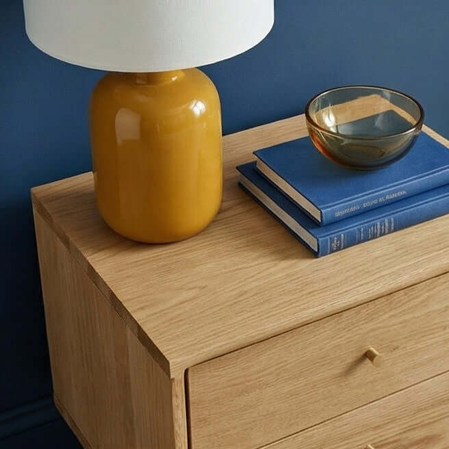 Fishe & Lilly Wright Oak Bedside Table with a minimalist wood finish, styled with a yellow lamp and blue books.