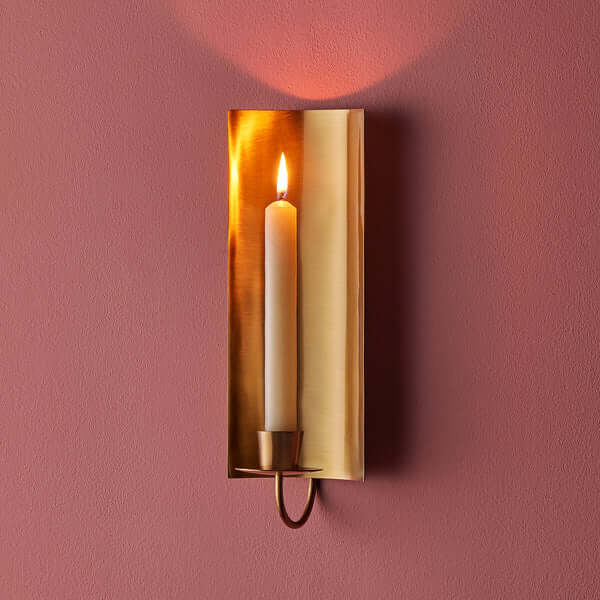 Pooky - Pitti Wall Mounted Candle Holder - Antiqued Brass with lit candle on a pink wall.