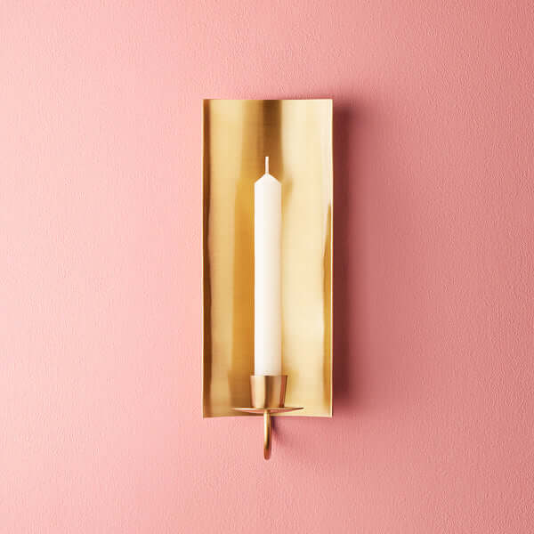 Pooky - Pitti Wall Mounted Candle Holder - Antiqued Brass mounted on a pink wall with a white candle.