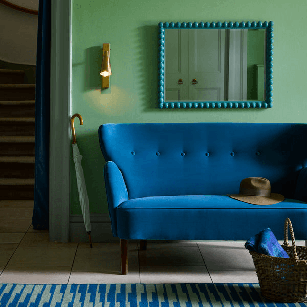 Pooky - Victor Wall Light - Antique Brass illuminating a stylish room with a blue sofa and green walls.