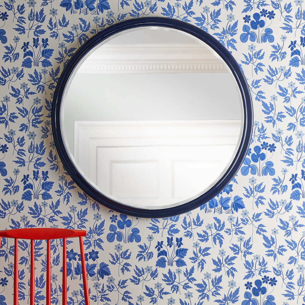 Pooky - Larger Cinders Mirror - Blue reflecting a floral blue patterned wall and a red wooden chair.