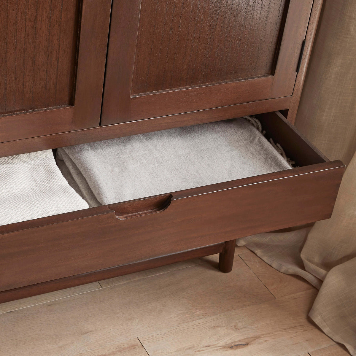 Open base drawer with folded blankets in the Fishe & Lilly Norway Dark Walnut Wardrobe.