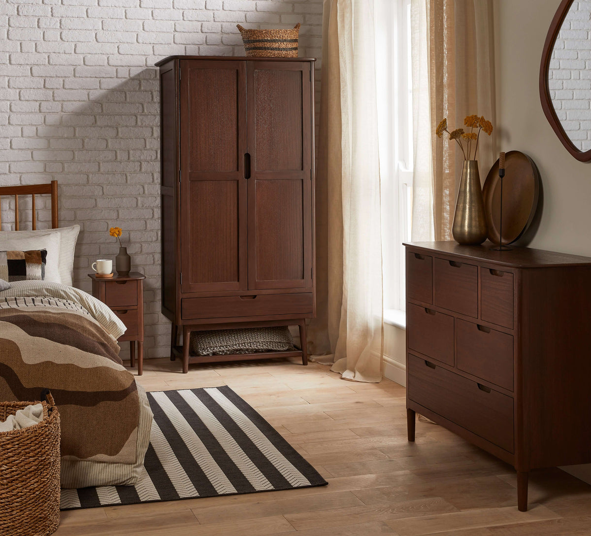 Fishe & Lilly Norway Dark Walnut Wardrobe in a modern bedroom setting with matching wood chest of drawers against a white brick wall.