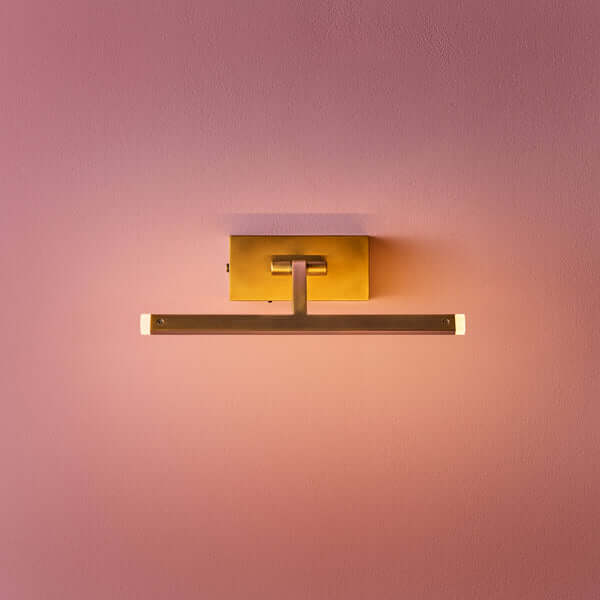 Pooky - Smaller Blake Rechargeable Picture Light - Brass mounted on a pink wall, showcasing its elegant design.