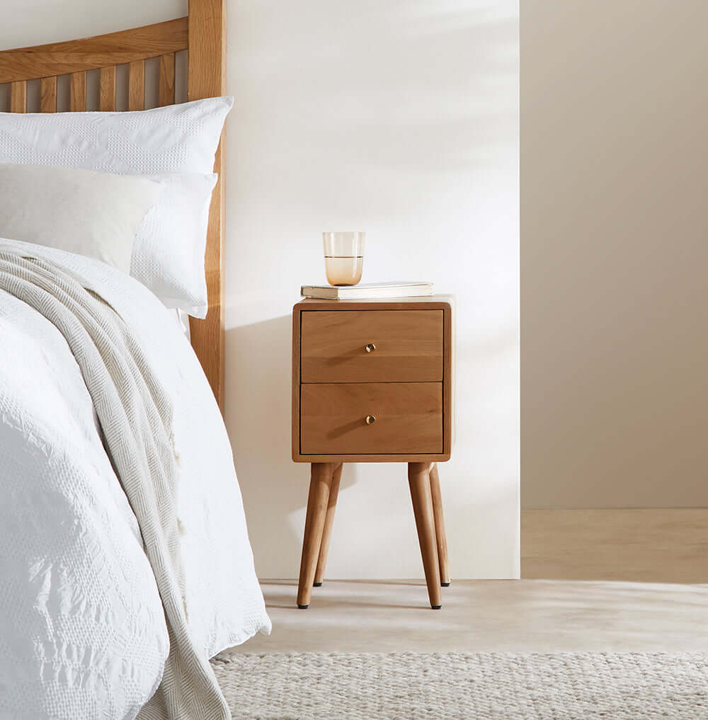 Fishe & Lilly Scandinavian Light Walnut Logan Narrow Bedside Table beside a white bed.