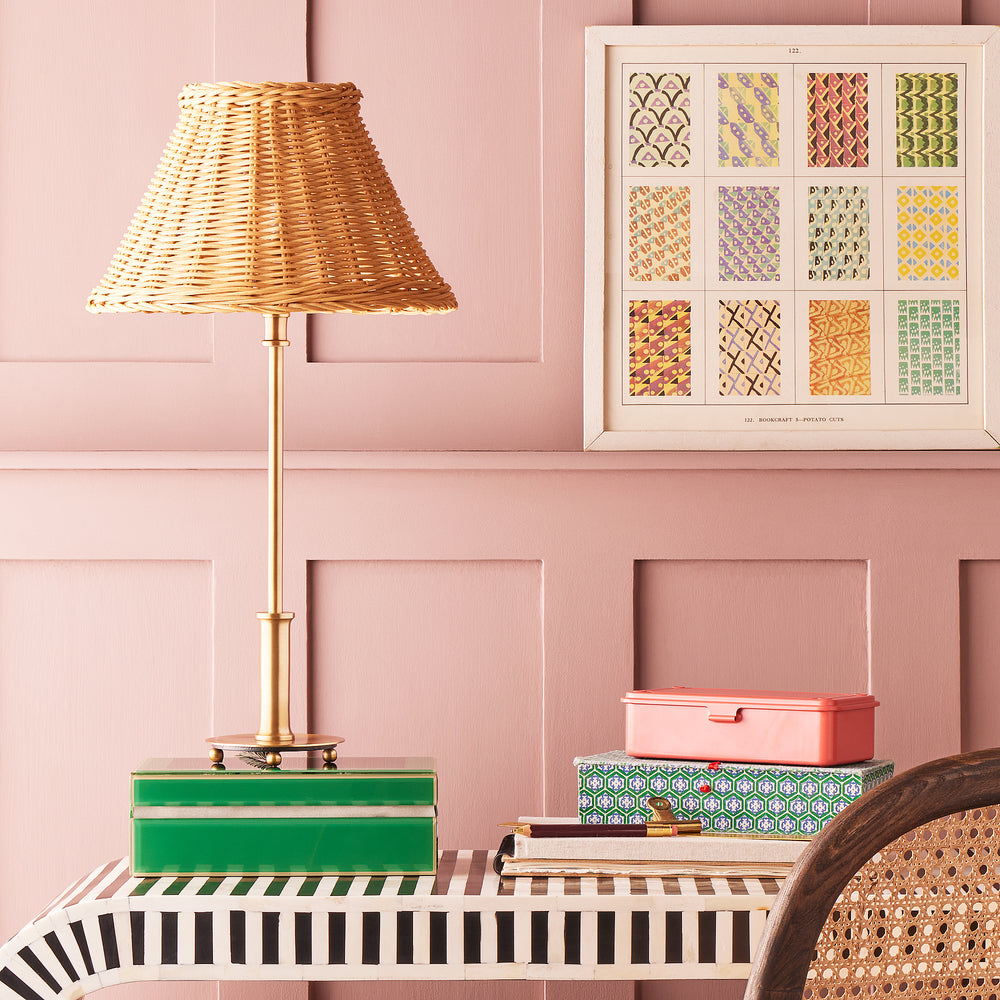 Pooky - Regular Pod Table Lamp Base - Antique Brass styled with a wicker shade against a pink wall.