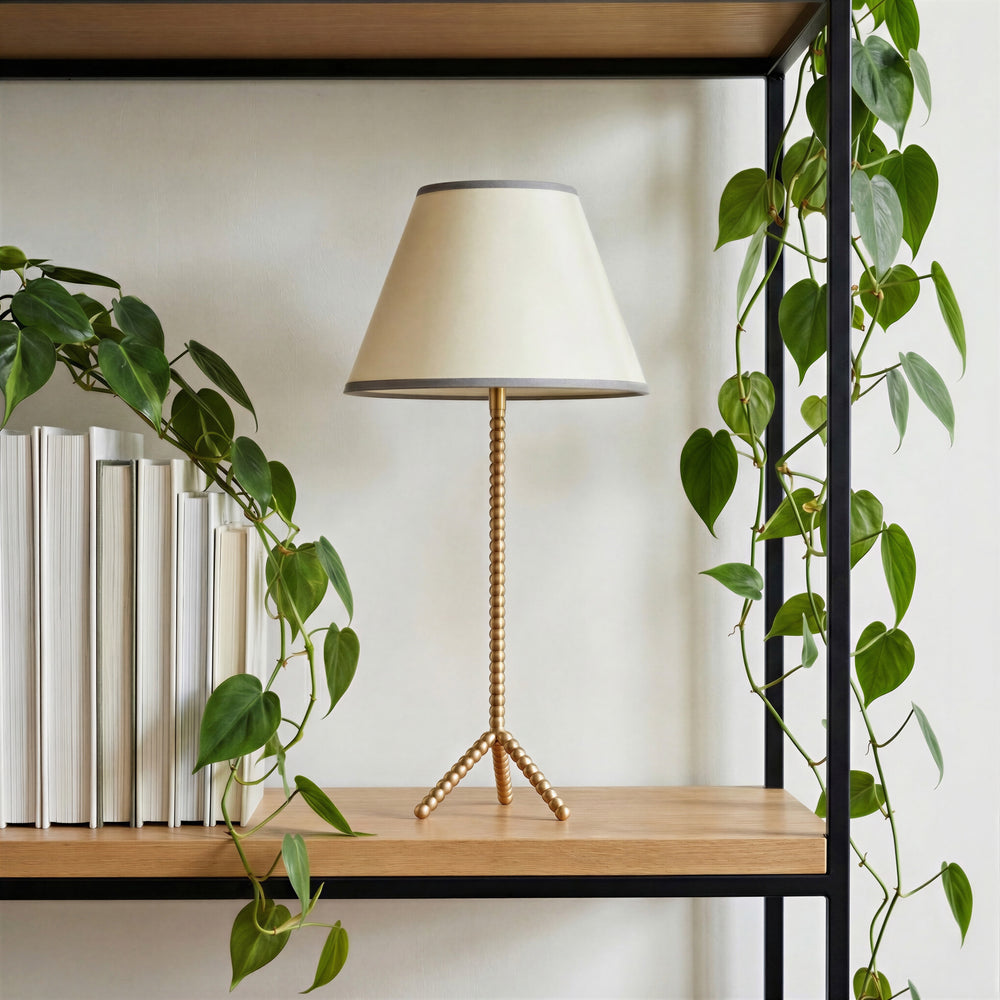 Pooky - Knobble Rechargeable Table Lamp Base - Brass on a wooden shelf with a plant.