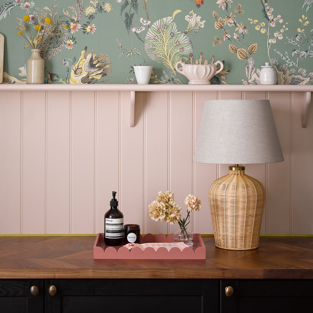 Pooky - Regular Rattle Table Lamp Base - Natural Cane with grey shade on a wooden counter against a pink wall.