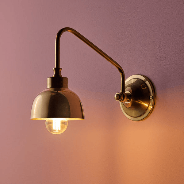Pooky - Carmel Wall Light - Antiqued Brass Finish displayed against a colored wall.