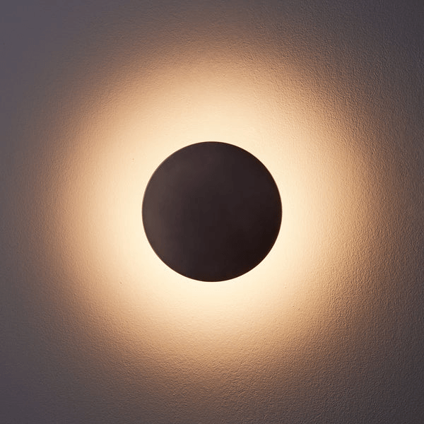 Pooky - Helios Ip44 Wall Light - Smaller - Brushed Bronze Aluminium illuminated on a wall, casting a warm glow.