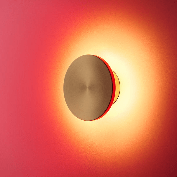Pooky - Helios Ip44 Wall Light - Smaller - Brushed Gold Aluminium on a pink wall, casting a warm glow.