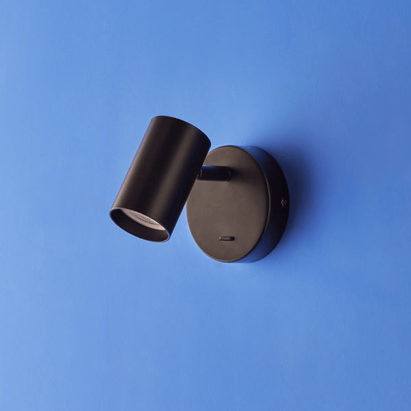 Pooky - Lewis single Wall Light - Black - With switch mounted on a blue wall, showcasing its sleek design.