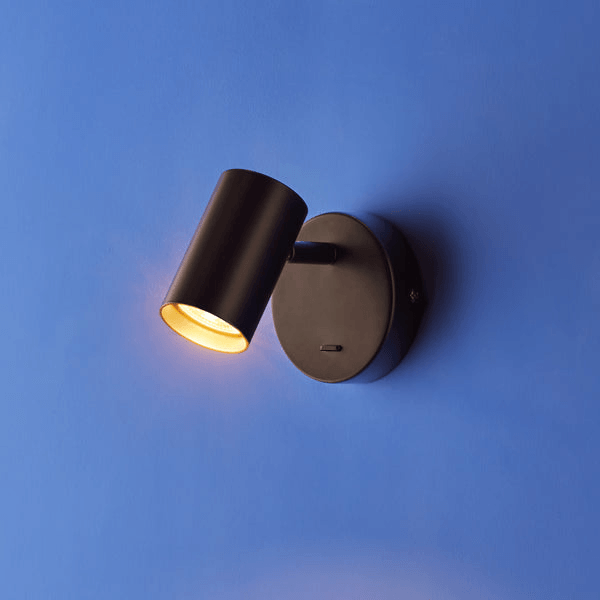 Pooky - Lewis single Wall Light - Black - With switch mounted on a blue wall, showcasing a cylindrical design.