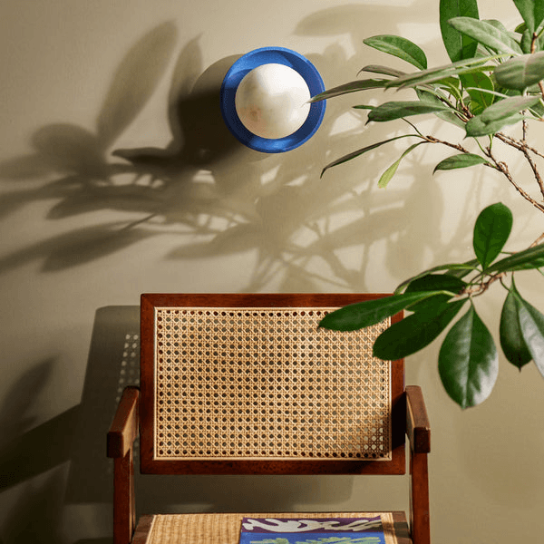Pooky - Luna Wall Light - Klein Blue mounted above a stylish wooden chair with a plant, adding contemporary elegance to the room.