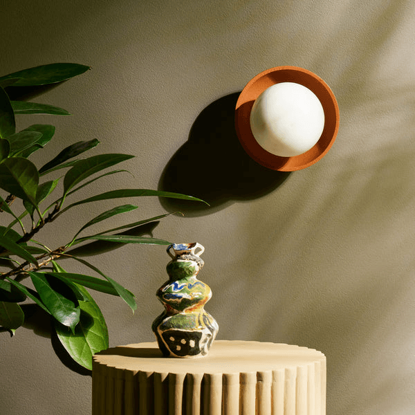 Pooky - Luna Wall Light - Terracotta Finish mounted on wall next to ceramic vase and plant