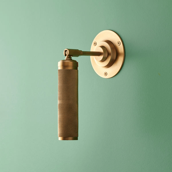 Pooky - Quantum Single Wall Light - Antiqued Brass featuring a knurled design on a green wall.