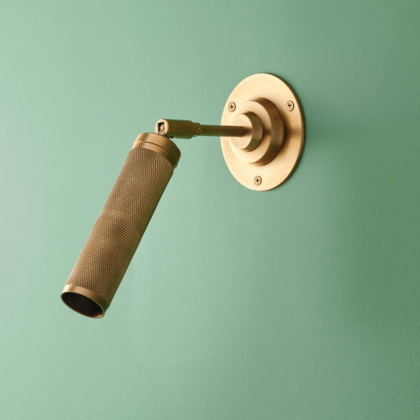 Pooky - Quantum Single Wall Light - Antiqued Brass mounted on a green wall with a knurled spotlight design.