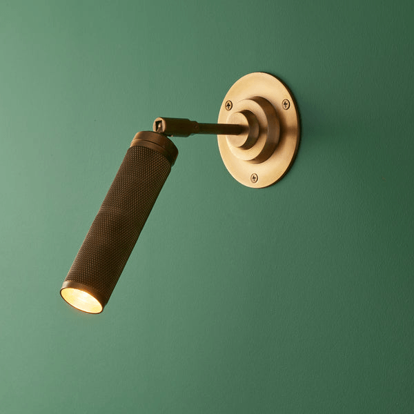 Pooky - Quantum Single Wall Light - Antiqued Brass mounted on green wall showcasing knurled design and warm light.