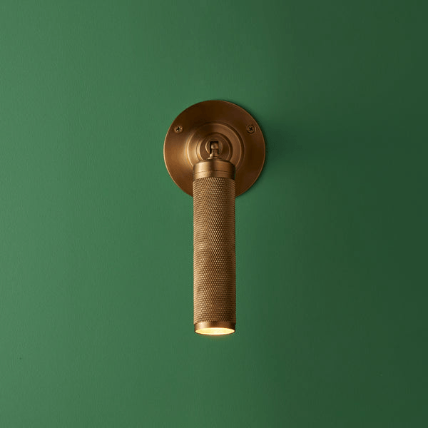 Pooky - Quantum Single Wall Light - Antiqued Brass mounted on green wall showcasing unique knurled design.