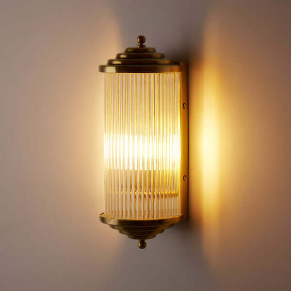 Pooky - Deco Baby Roddy ip44 Rated Wall Light - Brass and Glass illuminating a wall with warm light.