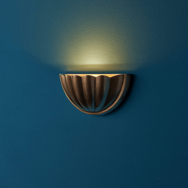 Pooky - St Jacques Wall Light - Smaller - Brass half-shell design wall sconce illuminated on a blue wall.