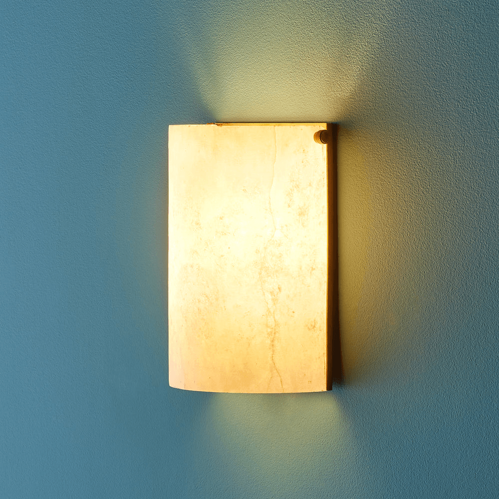 Pooky - Zeno Alabaster Wall Light illuminating a blue wall with its warm and natural glow.