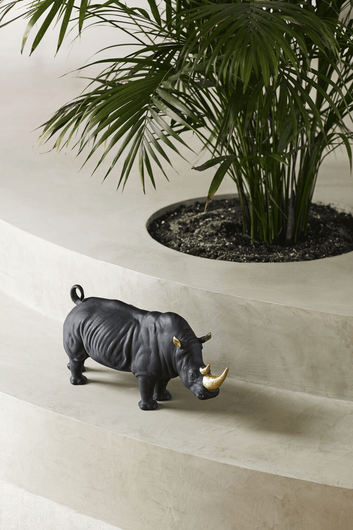 Lladró - Rhino Sculpture - Black-gold - Limited Edition displayed beside a plant in a modern setting.