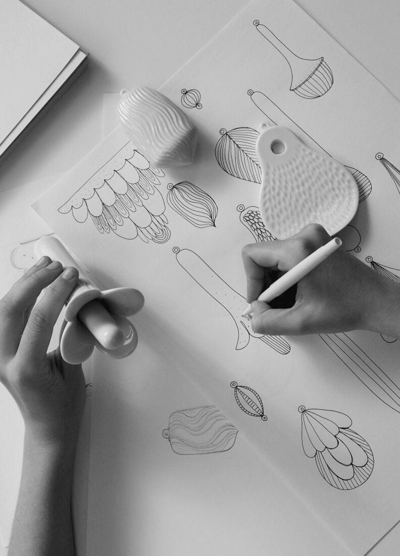 Artist sketching designs of Lladró porcelain pieces with white pencil on paper.
