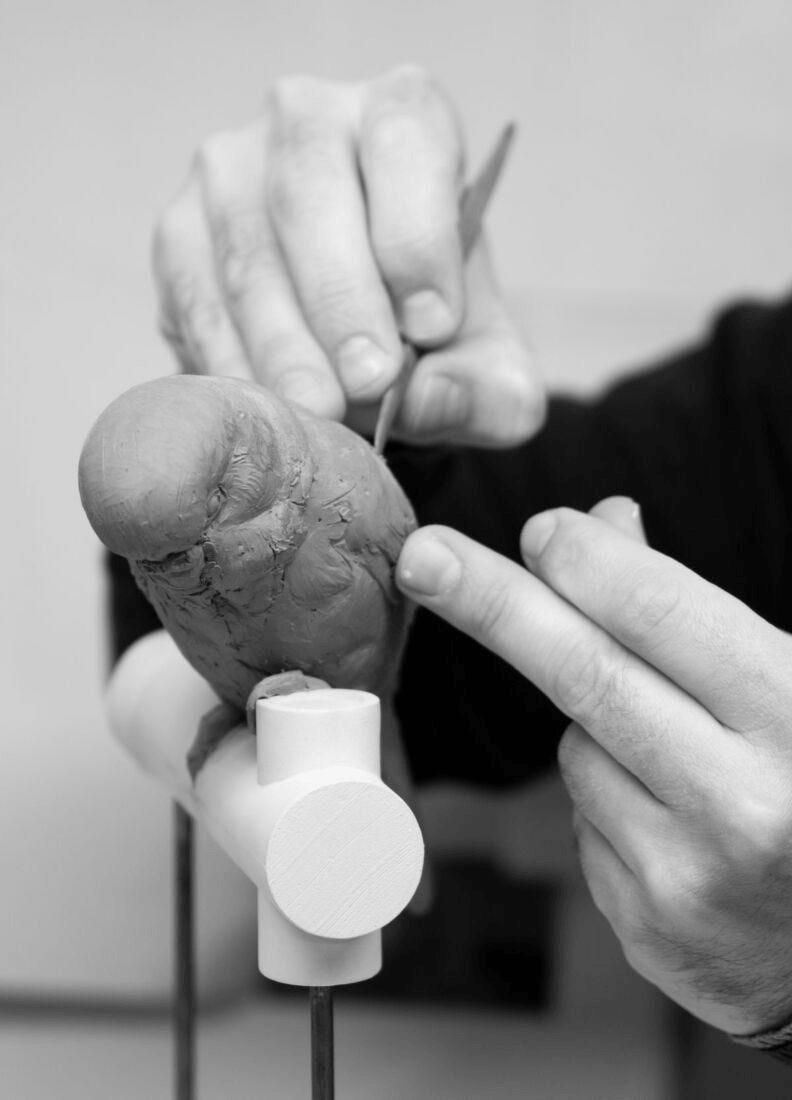 Artist sculpting a Lladró - Parrot Table Lamp - Black out of clay, showcasing intricate detailing in the design.