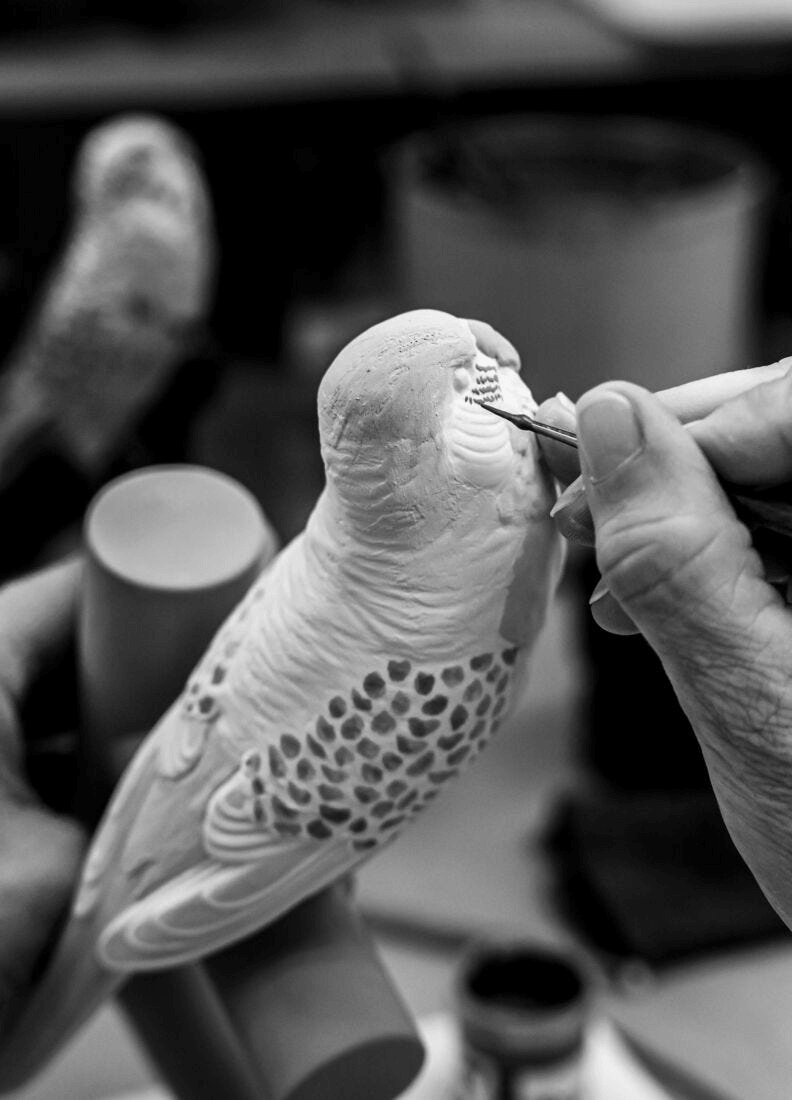 Craftsman painting details on a Lladró Parrot Table Lamp in progress, showcasing exquisite porcelain artistry.