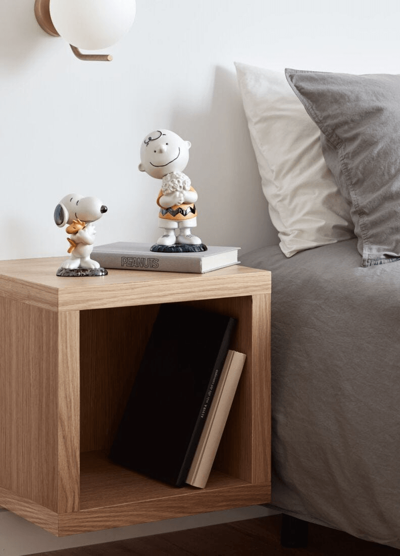 Lladró - Charlie Brown™ Figurine displayed on bedside table with Snoopy, featuring porcelain craftsmanship.