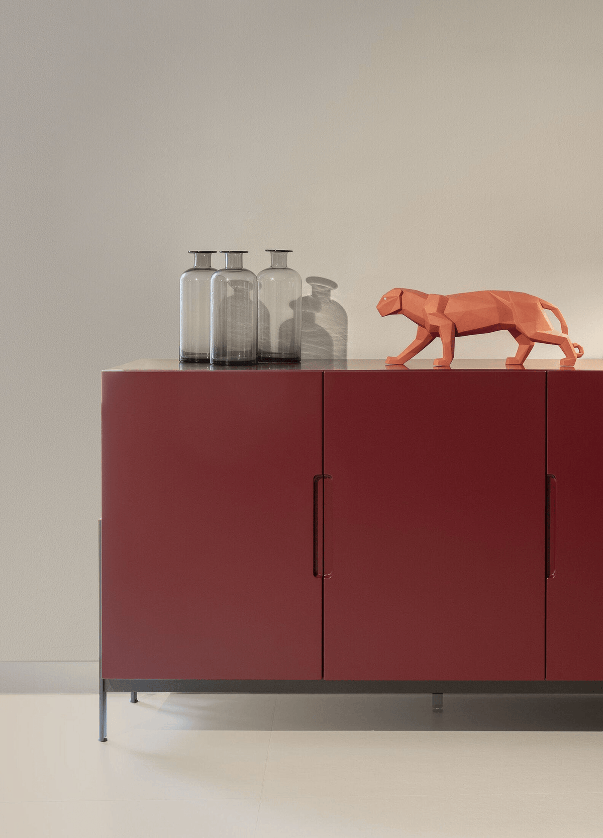 Lladró - Panther Sculpture - Coral Matte displayed on a cabinet with glass vases, showcasing its unique geometric design.