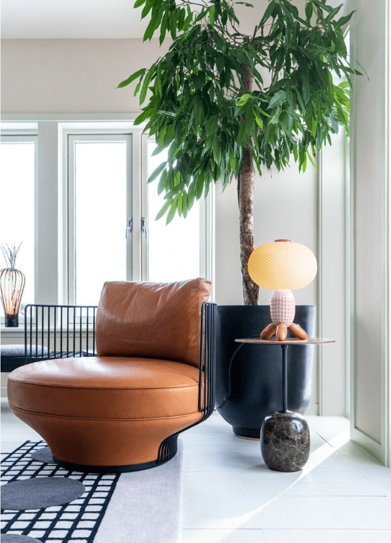 Lladró - Soft Blown Table lamp - Pink illuminating a cozy seating area with a leather chair and indoor plant.