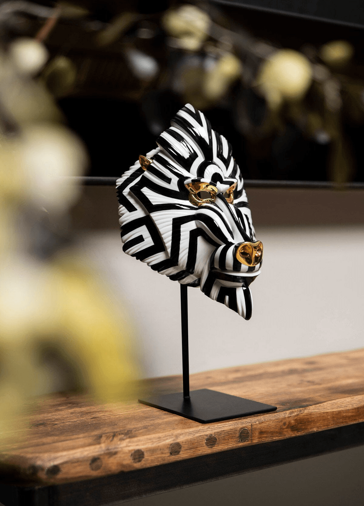 Lladró - Mandrill Mask - Black and Gold displayed on a stand with bold black and white design, highlighting porcelain craftsmanship.