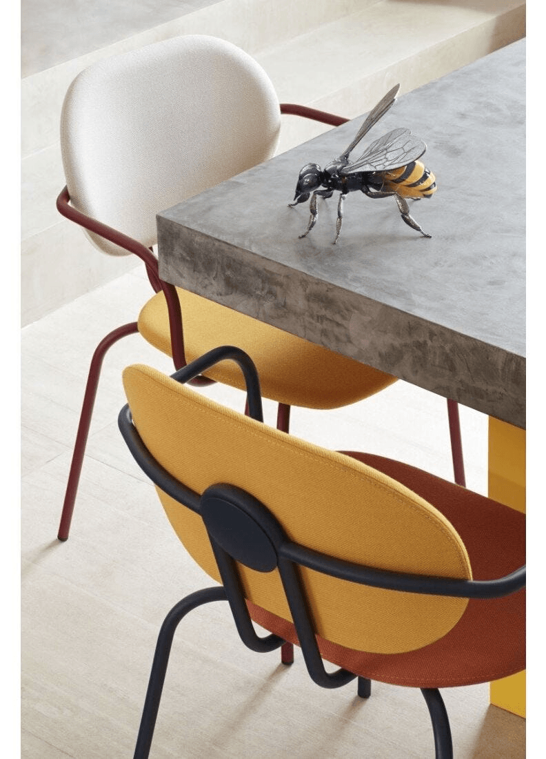 Lladró - Bee Sculpture placed on a modern table beside stylish chairs, showcasing its porcelain craftsmanship.