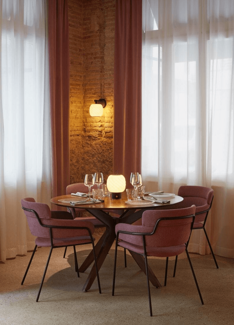 Lladró - Ice Cream Wall Sconce illuminating a cozy dining area with pink chairs and warm lighting.