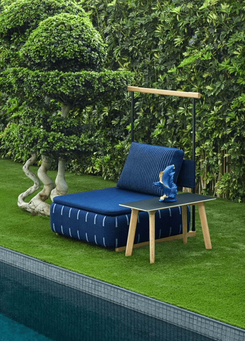 Outdoor seating with blue cushion and decorative fish sculpture, surrounded by greenery and pool.