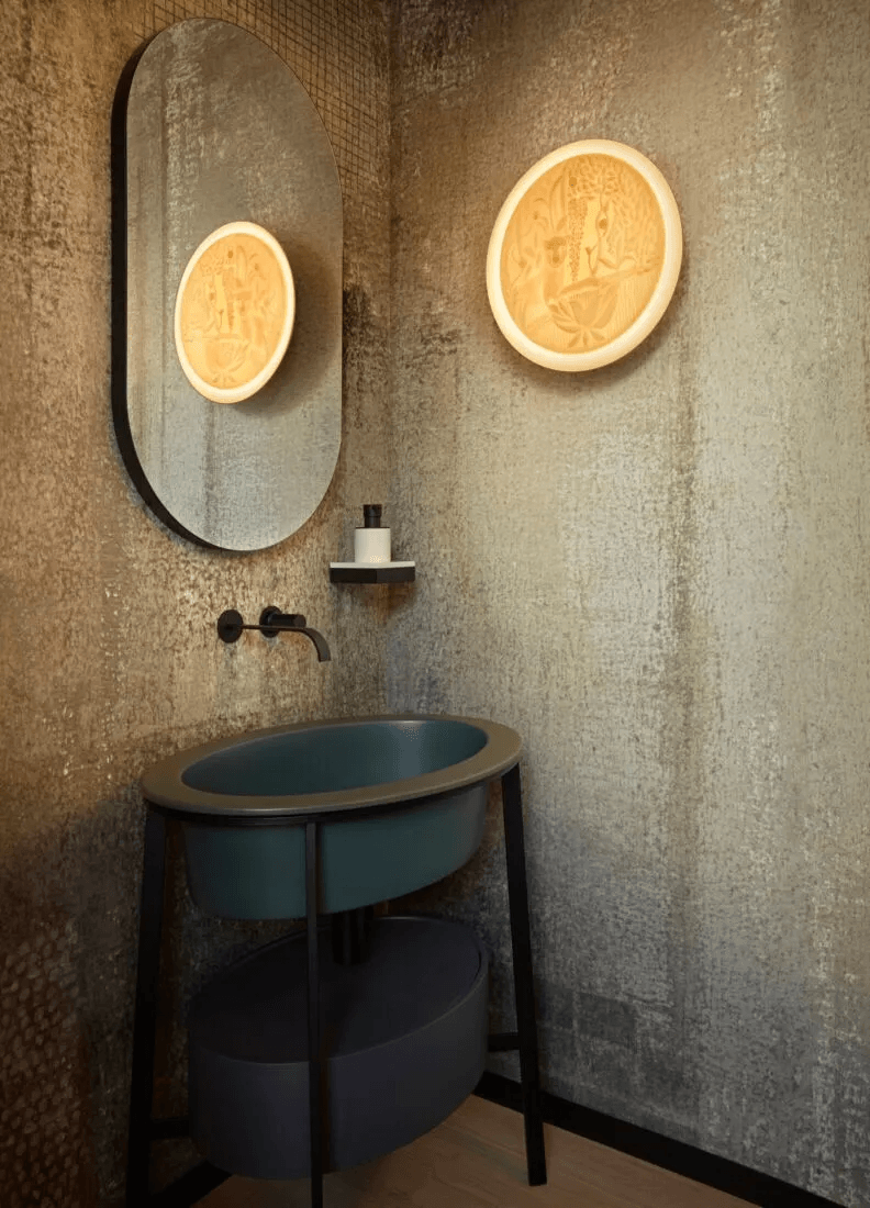 Lladró - Jungle wall light illuminating a contemporary bathroom with a round mirror and decorative elements.
