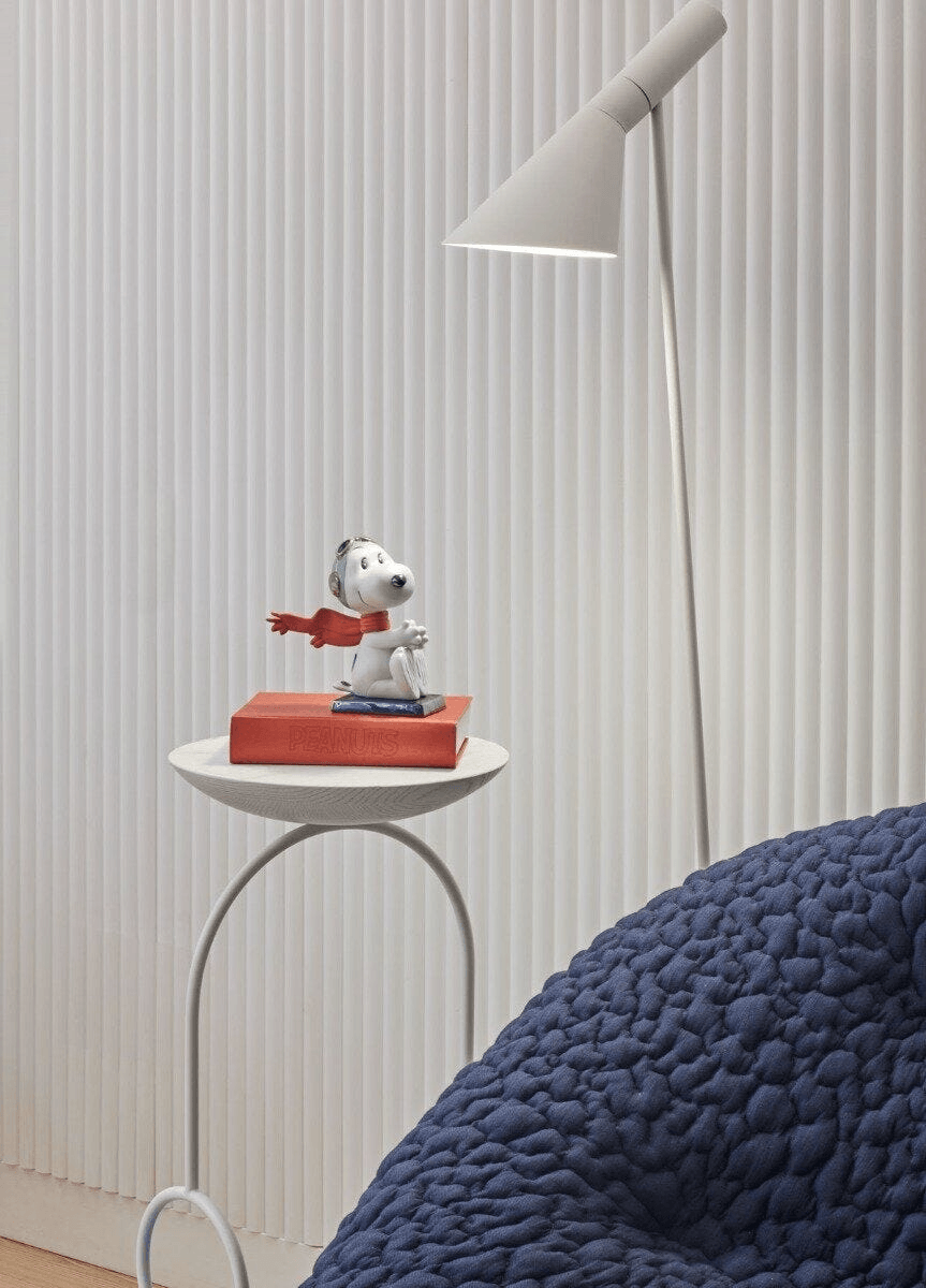 Lladró - Snoopy™ Flying Ace Figurine displayed on a table with a book and modern lamp, showcasing porcelain craftsmanship.