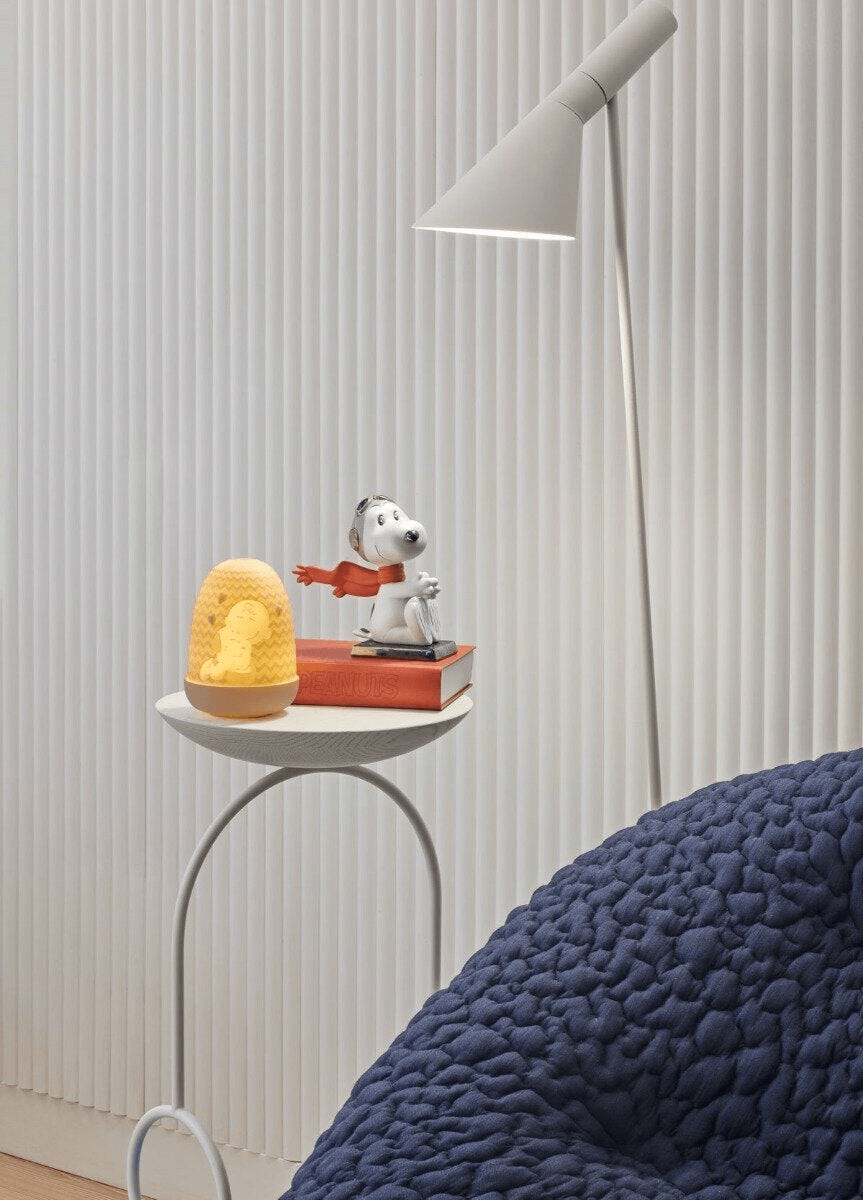 Lladró - Snoopy™ Flying Ace Figurine displayed on a table beside a lamp, perfect for collectors of porcelain art.