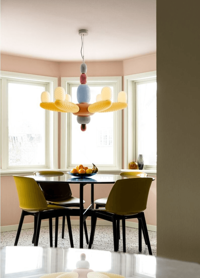 Lladró - Soft Blown Chandelier - Yellow hanging above a dining table with colorful chairs and fruit.