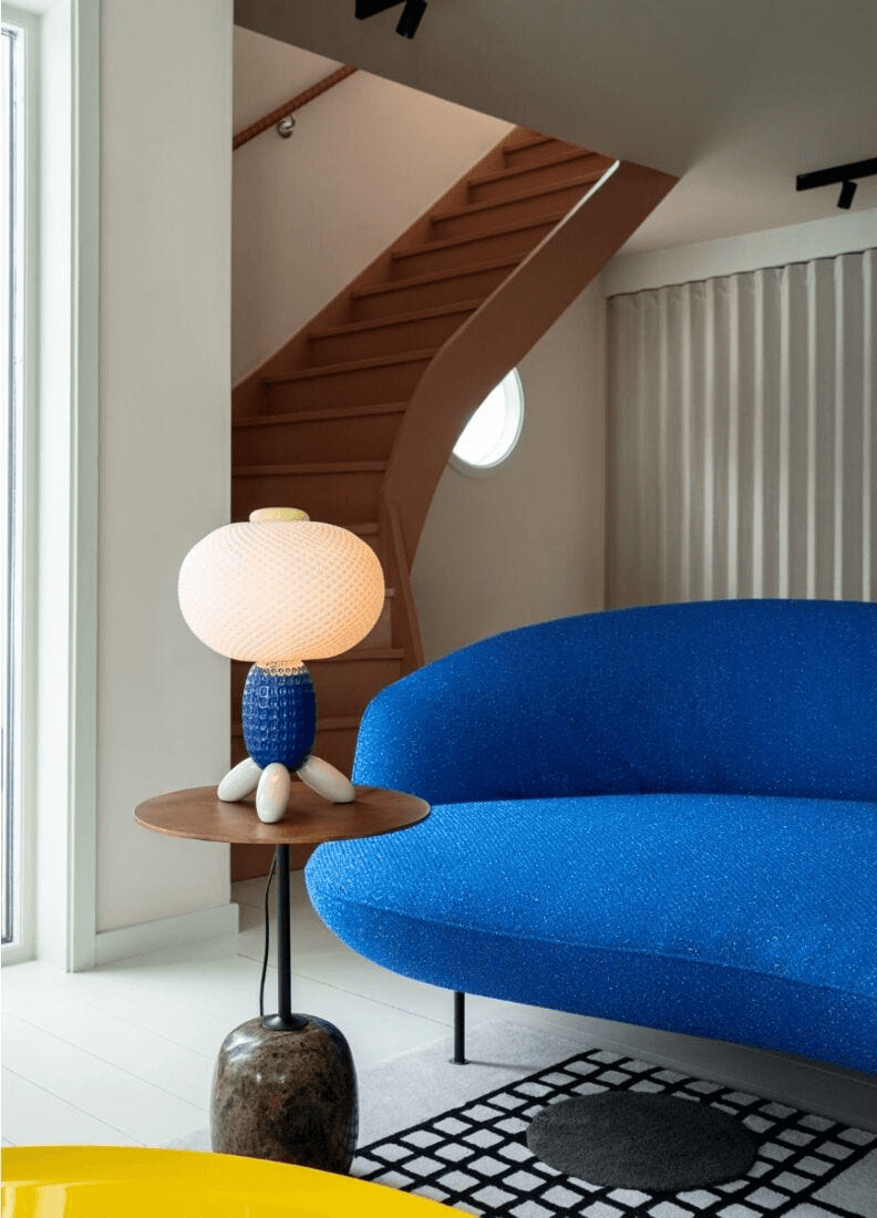 Lladro Porcelain decor featuring the Lladró - Soft Blown Table lamp - Blue on a side table next to a blue sofa.