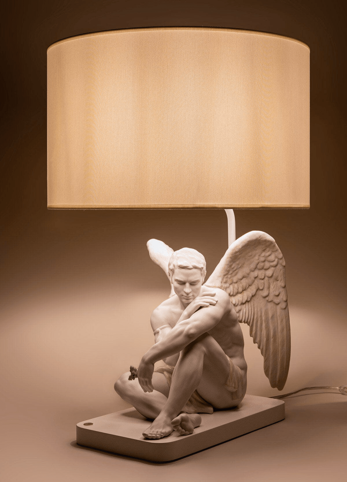 Lladró - Protective Angel Table Lamp in white Porcelain. This Lladro sculpture features a seated winged male angel and a beige shade.