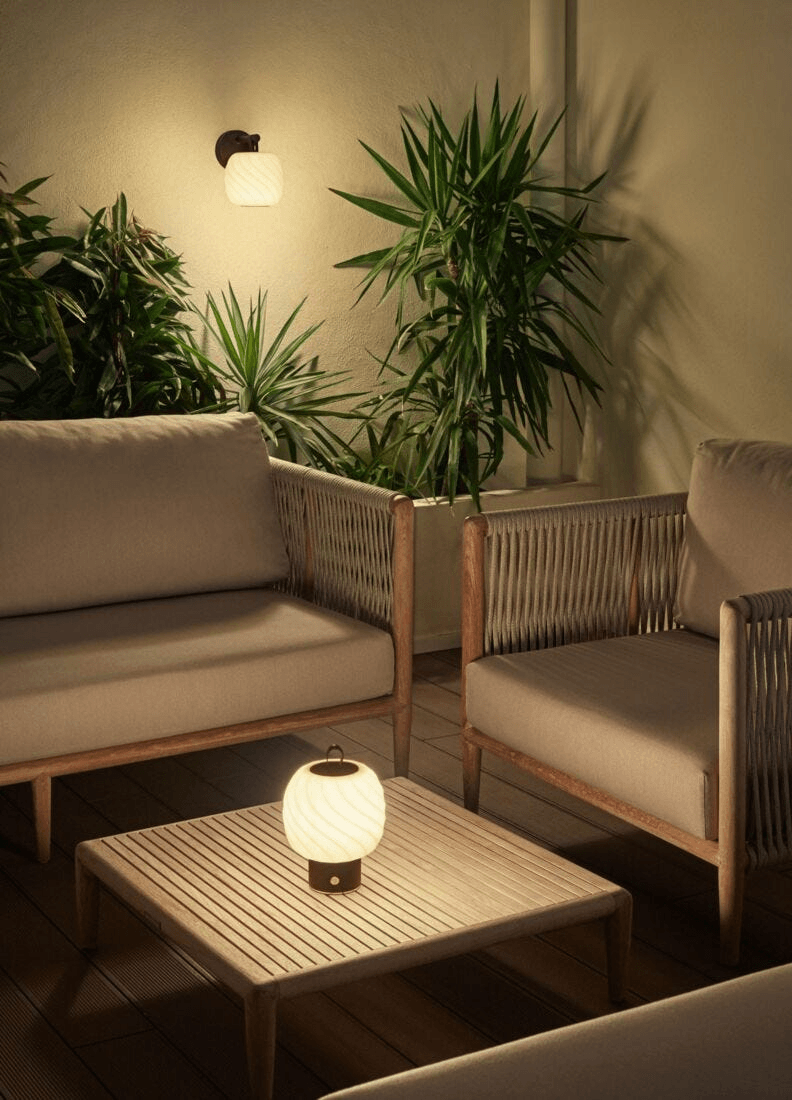 Lladró - Ice Cream Wall Sconce illuminating a cozy outdoor seating area surrounded by greenery.