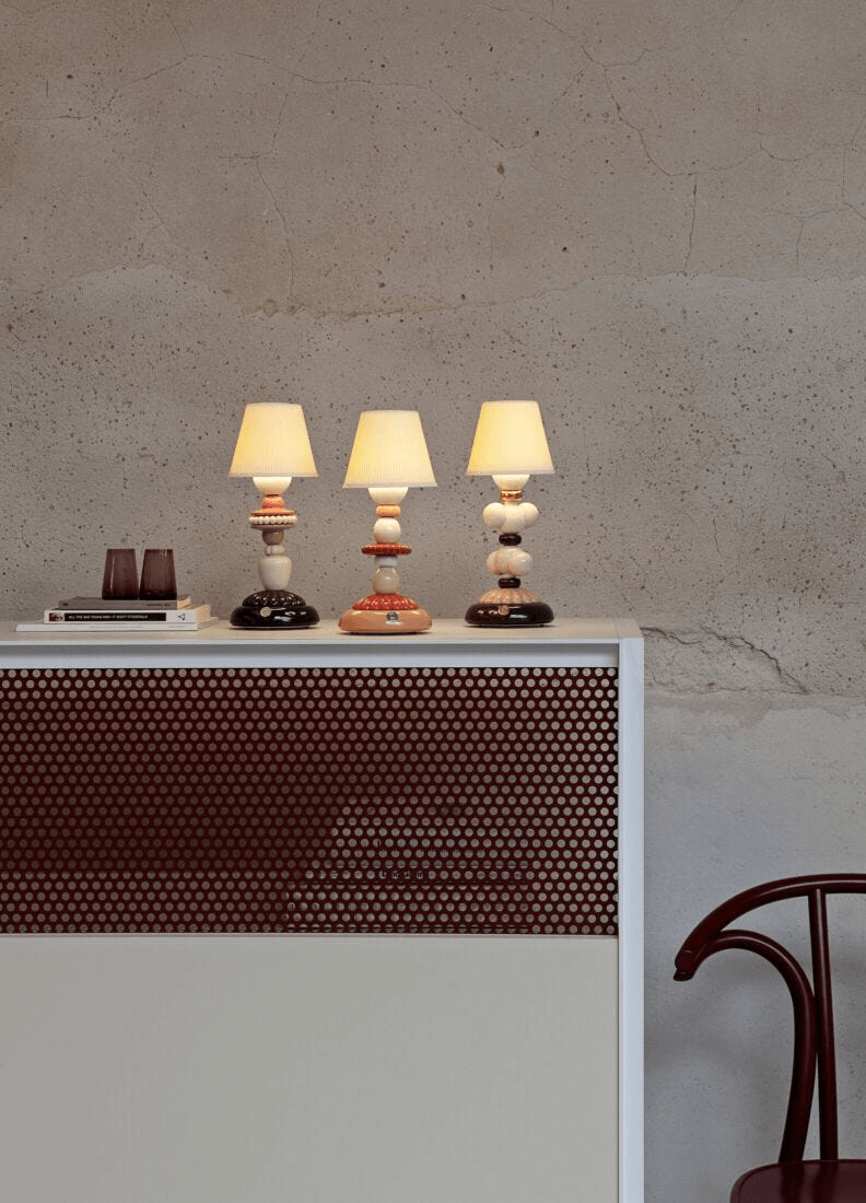 Lladró - Lotus Firefly Table Lamp - Coral displayed elegantly among decorative items on a modern furniture piece.