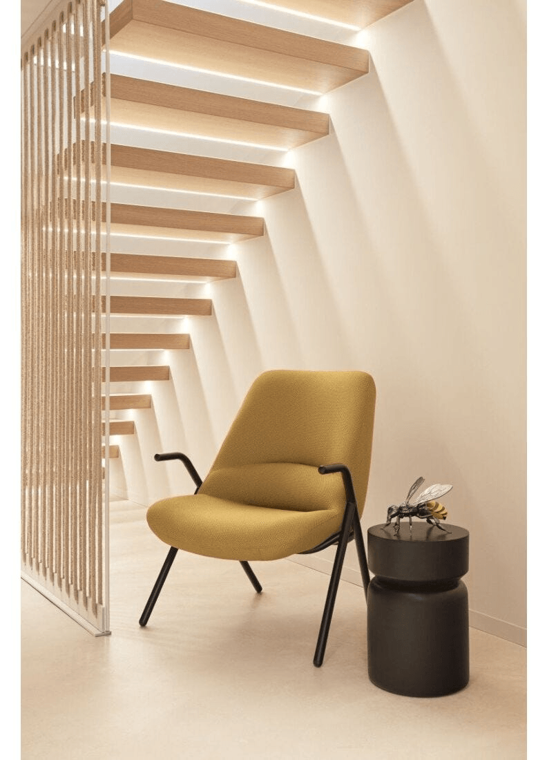 Lladró - Bee Sculpture displayed on a black table next to a mustard yellow chair in a modern interior.