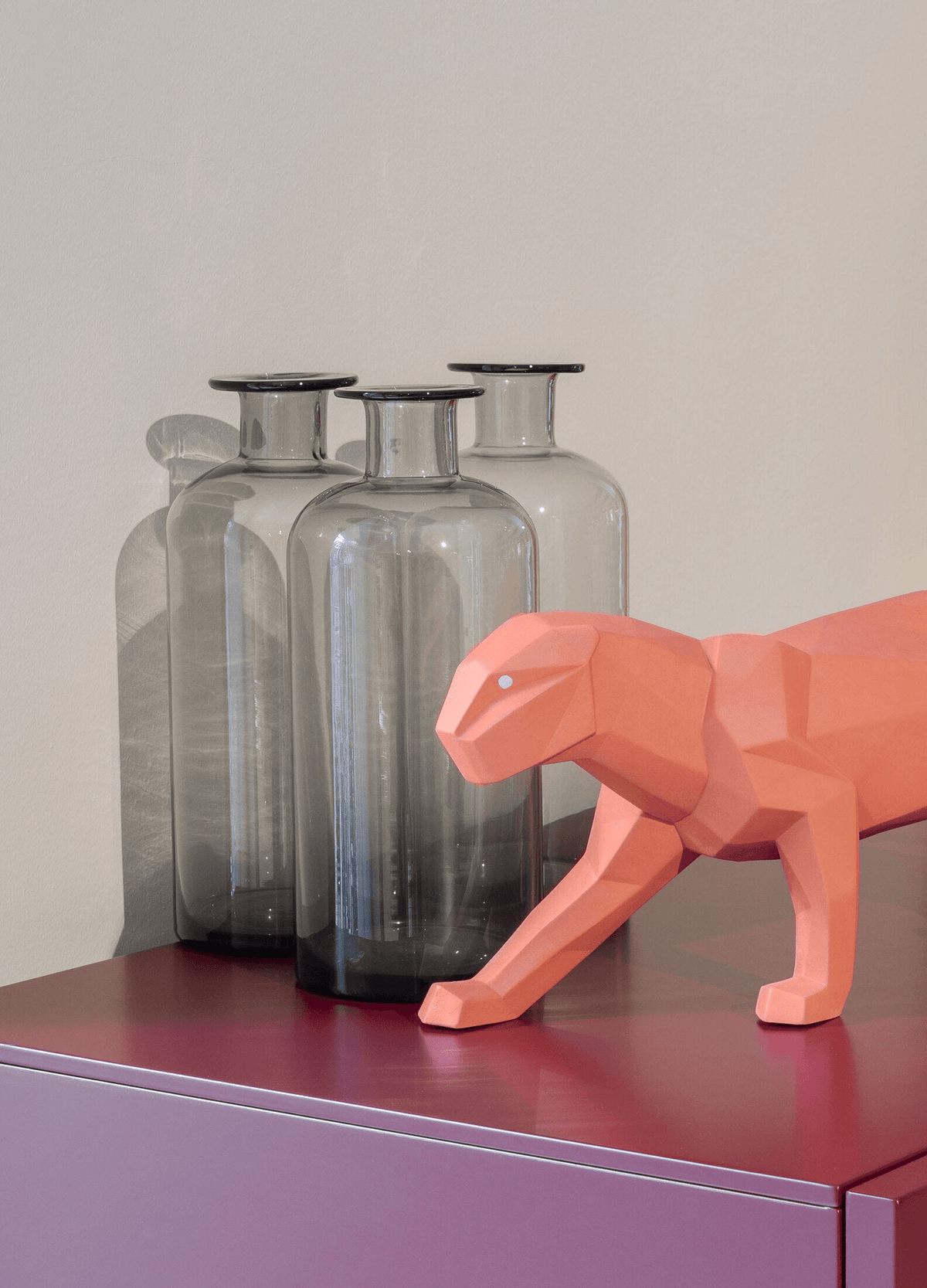 Lladró - Panther Sculpture - Coral Matte beside glass vases on a colorful surface.