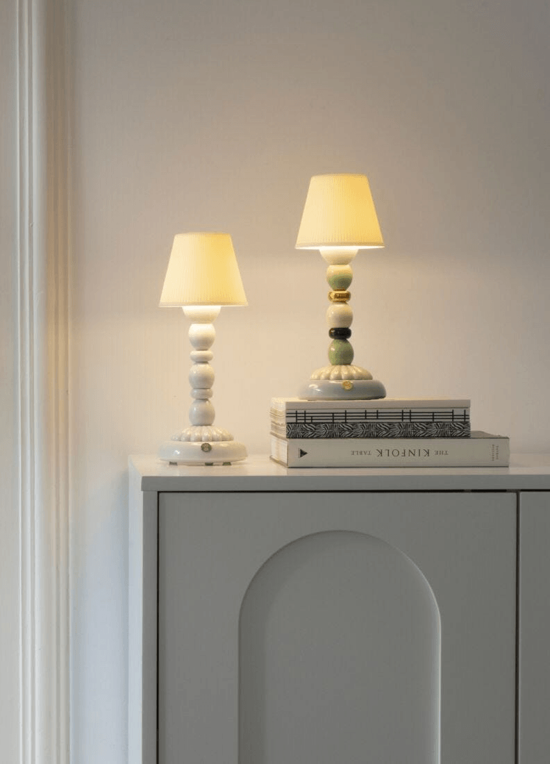 Lladró - Palm Firefly Table Lamp - White atop a bookshelf with books and subtle lighting.
