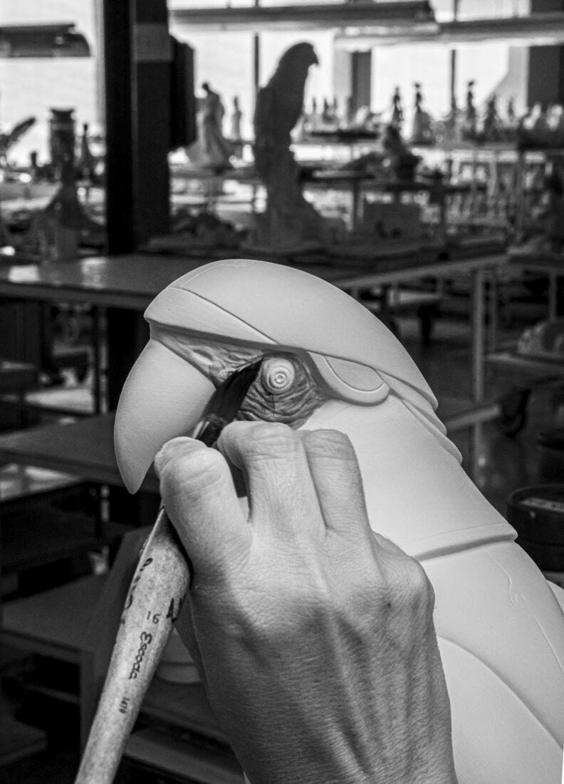 Artisan sculpting the Lladró - Macaw bird Cyborg Sculpture in a workshop with detailed features.